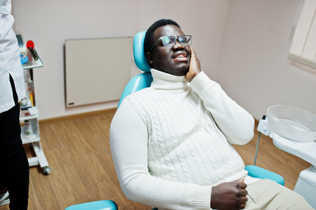 African american man having toothache sitting in a dental chair and need helping, male patient in pain. Dentistry medical.の写真素材
