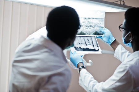 Dentist office and doctor practice concept. Professional african american doctor at dentistry medical pointing on teeth X-ray.の写真素材