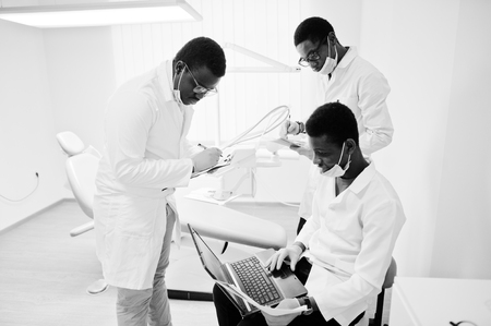 Three african american male doctors working with laptop, discussing with colleagues in dental clinic.の写真素材