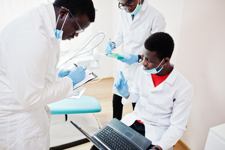 Three african american male doctors working with laptop, discussing with colleagues in dental clinic.の写真素材