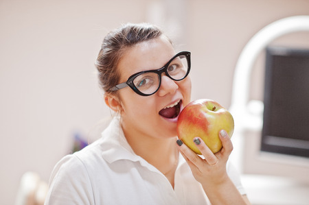 Portrait of female dentist woman standing in her dentistry office and eating an apple.の写真素材