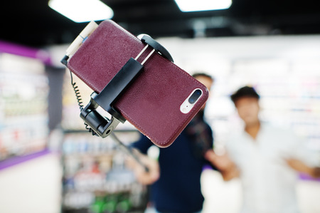 Close up photo of mobile phone on monopod stick against two indians mans customer buyer aking...