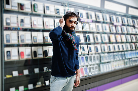 Indian beard man customer buyer at mobile phone store with wireless earphones. South asian peoples...