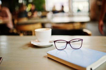 Close up photo of notebook with glasses against cup of coffe at cafe table. Eyewear concept.の写真素材