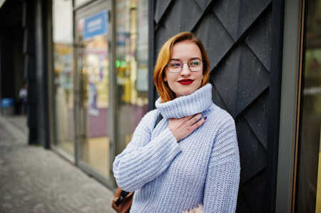 Cheerful young beautiful redhaired woman in glasses, warm blue wool sweater with backpack posed...