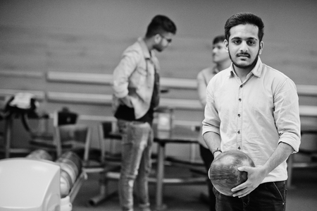 South asian man in jeans shirt standing at bowling alley with ball on hands. Guy is preparing for a throw.の写真素材