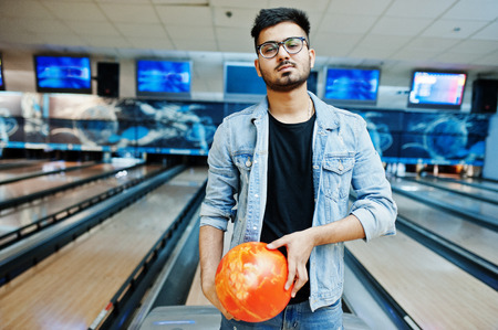 Stylish beard asian man in jeans jacket and glasses standing at bowling alley with ball at hand.の写真素材