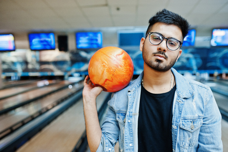 Stylish beard asian man in jeans jacket and glasses standing at bowling alley with ball at hand.の写真素材