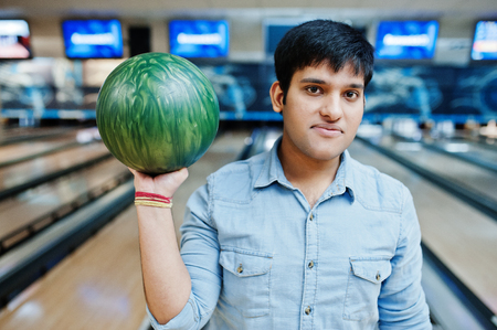 Stylish asian man in jeans shirt standing at bowling alley with ball at hand.の写真素材