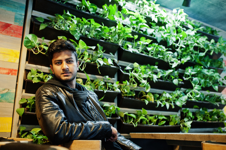 Casual and stylish young asian man wear on leather jacket sitting at cafe against green plant.