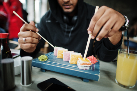 Casual and stylish young asian man on hood at cafe eating sushi.の写真素材