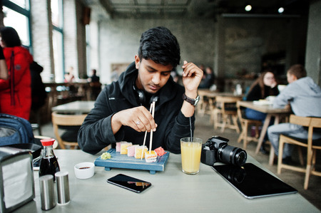 Casual and stylish young asian man with earphones at cafe eating sushi.の写真素材