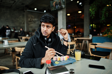 Casual and stylish young asian man with earphones at cafe eating sushi.の写真素材