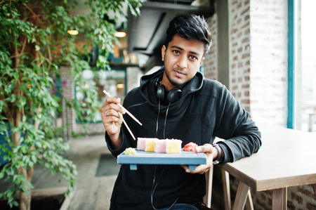 Casual and stylish young asian man with earphones at cafe eating sushi.の写真素材