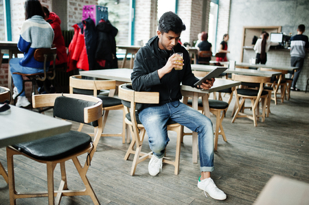 Casual and stylish young asian man with earphones at cafe drinking juice from glass and holding tablet.の写真素材
