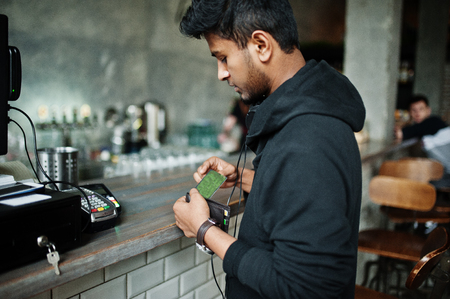 Casual and stylish young asian man with earphones at cafe on bar paying by credit card on pos terminal.の写真素材