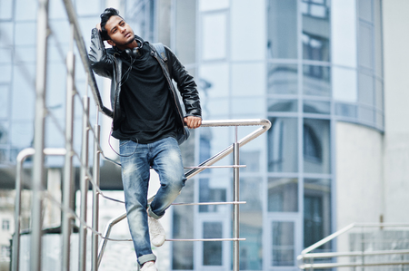 Stylish and casual asian man in black leather jacket posed near the railing against modern building.の写真素材