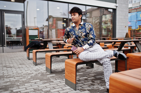 Attractive and handsome stylish indian man wear on shirt, holding mobile phone and sitting in the terrace of modern lounge cafe at his work break.の写真素材
