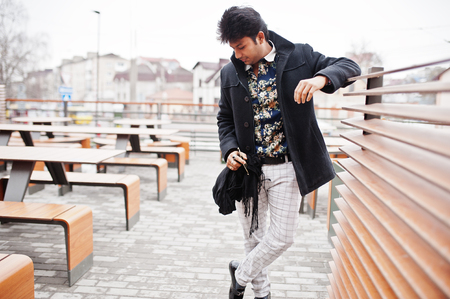 Attractive and handsome stylish indian man wear on black coat standing in the terrace of modern lounge cafe at his work break.の写真素材