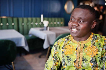 Close up portrait of friendly afro man in traditional yellow clothes sitting at restaurant.の写真素材