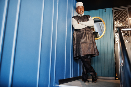 African men in black traditional clothes with cap against mirror on blue wall.の写真素材