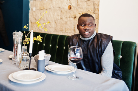 African man in black traditional clothes sitting at restaurant with glass of red wine.の写真素材