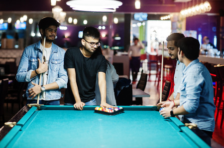 Group of stylish asian friends wear on jeans playing pool billiard on bar.