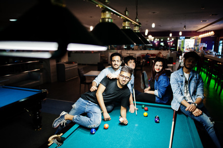 Group of stylish asian friends wear on jeans playing pool billiard on bar.