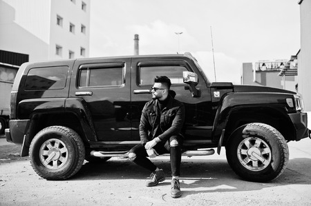 Fashion rich beard Arab man wear on black jeans jacket and sunglasses posed against big black suv...
