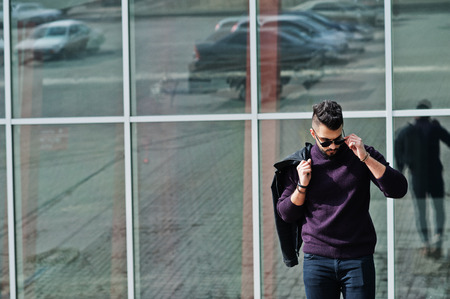 Fashion rich beard Arab man wear on turtle neck and sunglasses posed against large windows of modern...
