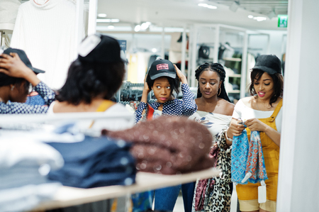 Three african woman choosing clothes at store. Shopping day. They buying caps and scarfs and looking at mirror.の写真素材