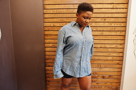 Casual african woman in jeans shirt and shots clothes posing against wooden wall.の写真素材