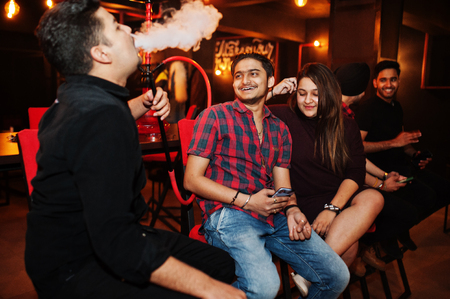 Group of indian friends sitting at lounge bar, smoke hookah and having rest.