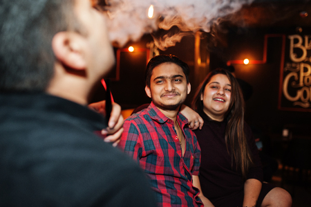 Group of indian friends sitting at lounge bar, smoke hookah and having rest.の写真素材