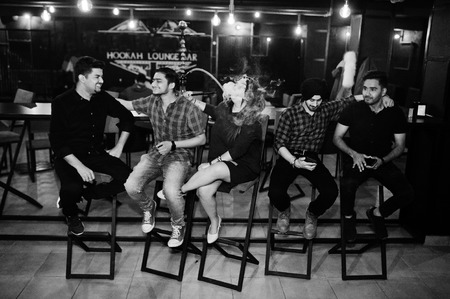 Group of indian friends sitting at lounge bar, smoke hookah and having rest.の写真素材