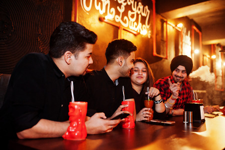 Group of indian friends having fun and rest at night club, drinking cocktails and smoke hookah.