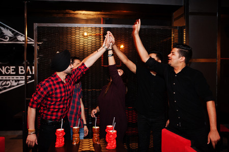Group of indian friends having fun and rest at night club, drinking cocktails and giving high five...