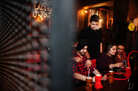 Group of indian friends having fun and rest at night club, drinking cocktails and smoke hookah,...