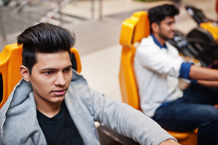 Two asian guys compete on speed rider arcade game racing simulator machine.の写真素材