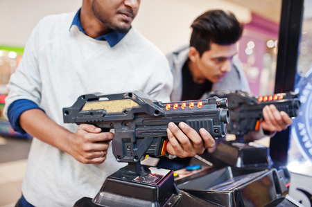 Two asian guys compete on shooter simulator game arcade machine.