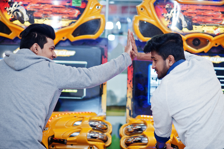 Two asian guys compete on speed rider arcade game motorcycle racing simulator machine. Give high five each other.の写真素材