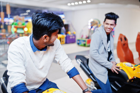 Two asian guys compete on speed rider arcade game motorcycle racing simulator machine.の写真素材