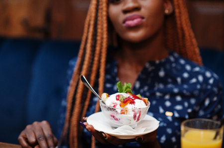 Close up portrait of beautiful young african business woman with dreadlocks, wear on blue blouse, sitting in cafe with ice cream and pineapple juice.の素材 [FY310120998135]