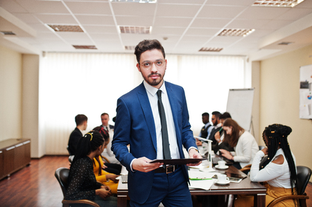 Face of handsome arabian business man, holding clipboard on the background of business peoples multiracial team meeting, sitting in office table.の写真素材