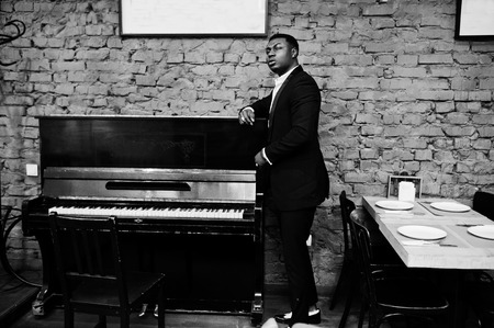 Strong powerful african american man in black suit standing against piano.の写真素材