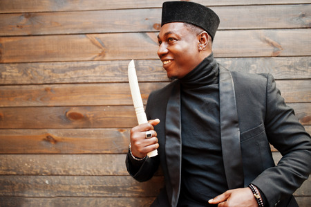Strong powerful african american man in black suit and turtleneck and cap, with elephant tusk.の写真素材