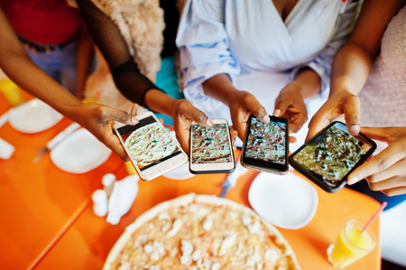 Close up photo of four young african girls making photo of pizza in their mobile phones.の写真素材