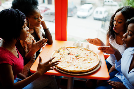 Four young african girls in bright colored restaurant sniffing pizza and having fun together.の写真素材