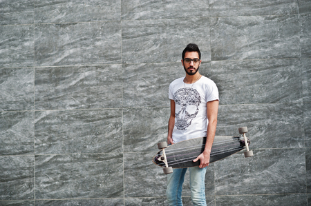 Street style arab man in eyeglasses with longboard posed against gray wall.の写真素材