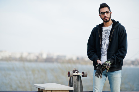 Street style arab man in eyeglasses with longboard posed against river.の写真素材